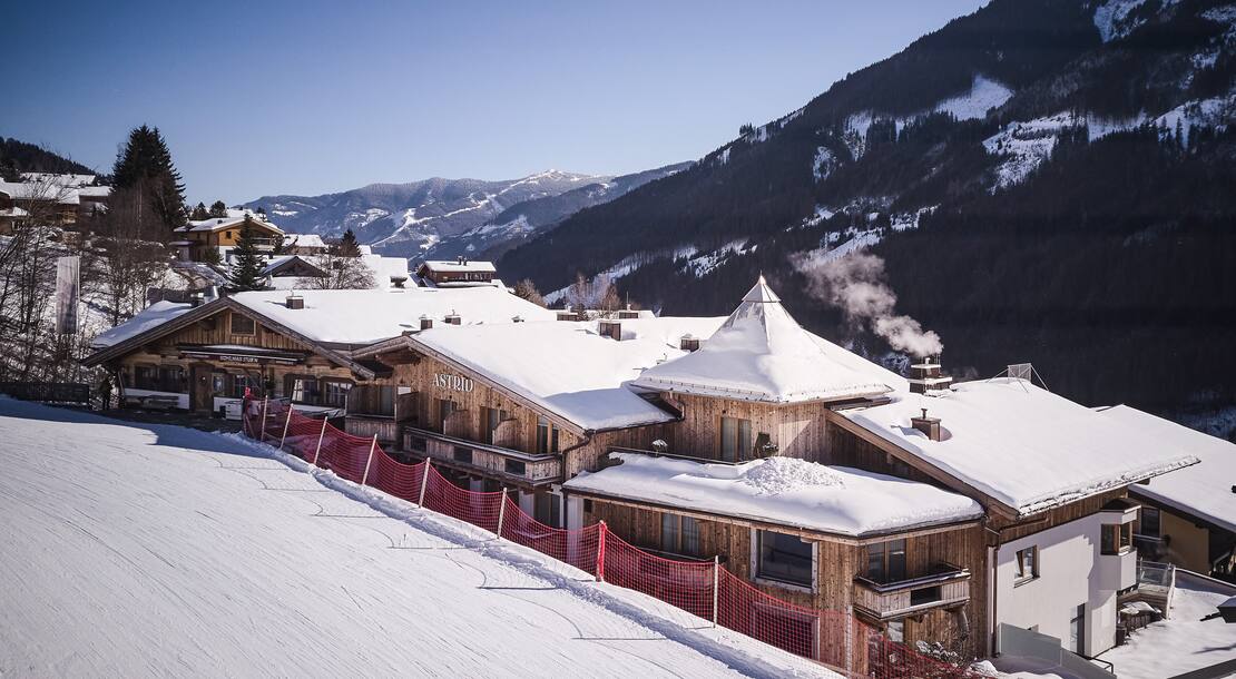 Aussenansicht des Hotel Astrid im Winter mit der Skipiste, die direkt am Hotel entlang führt 