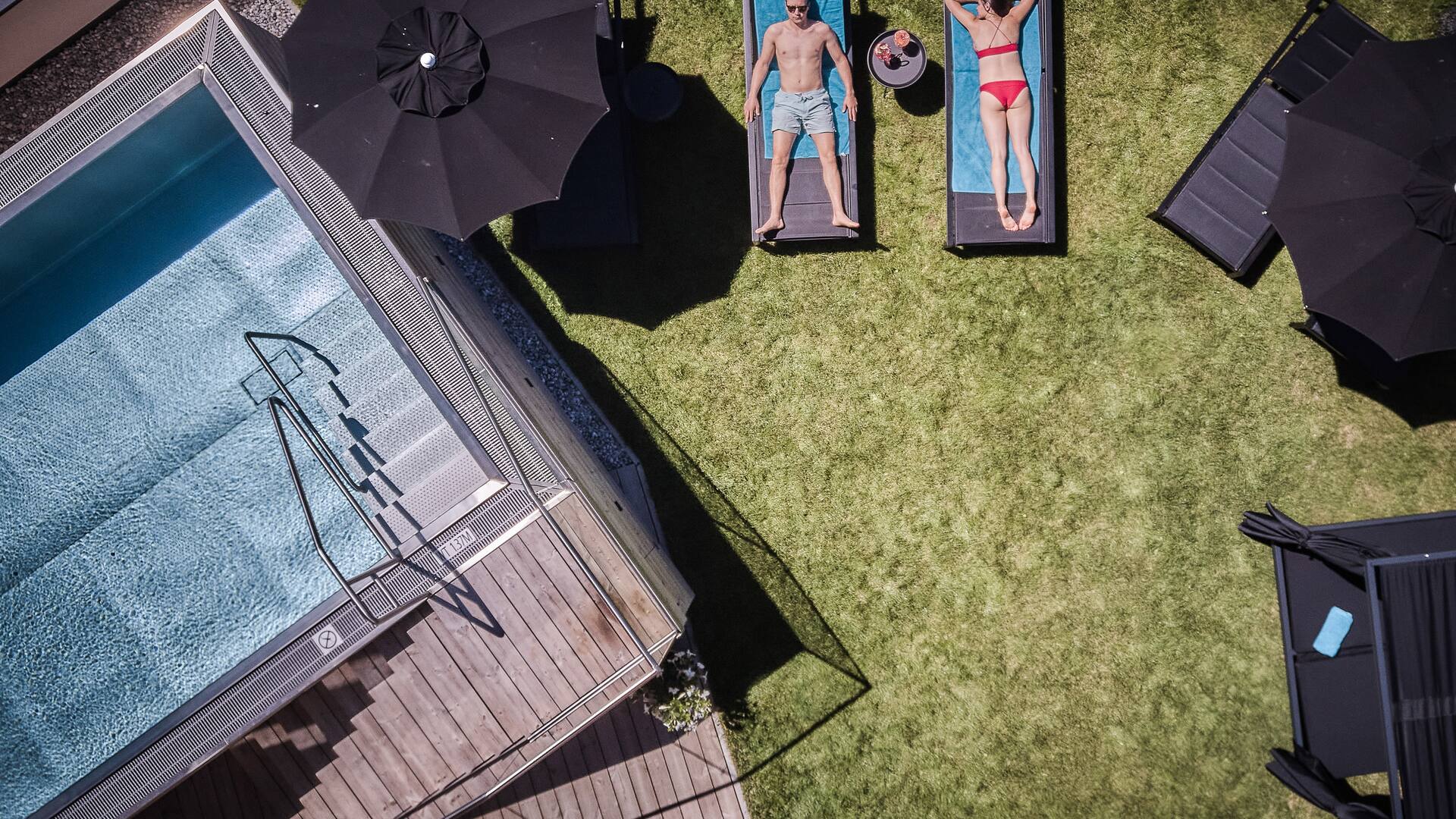 Pärchen sonnt sich auf Sonnenliegen neben dem Outdoorpool im Garten des Hotel Astrid 