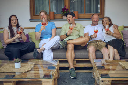 Familie Steger sitzt gemütlich beisammen in der Lounge, genießt Aperol und die sommerliche Atmosphäre