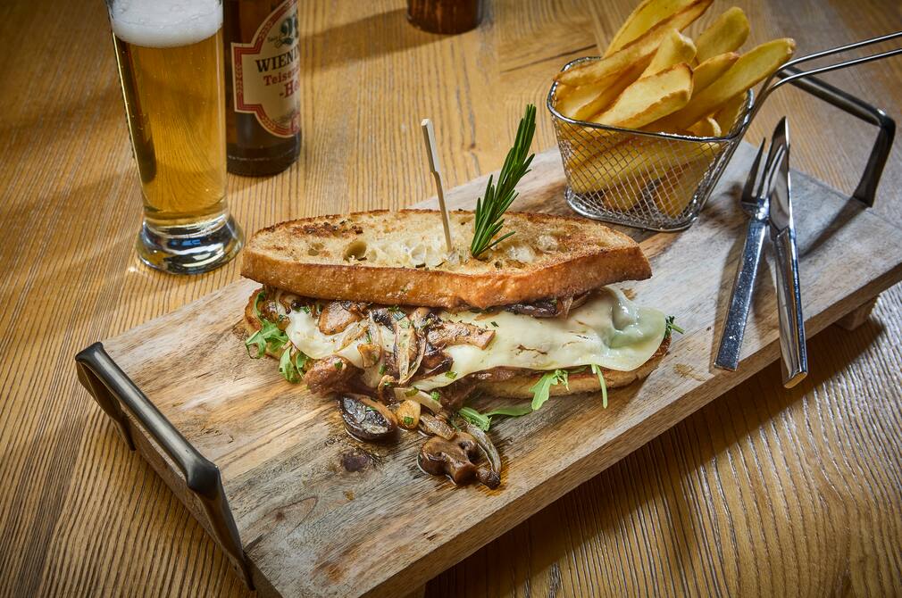 Getoastetes Landbrot mit geschmolzenem Käse, Rucola und Champignons, serviert mit hausgemachten Pommes